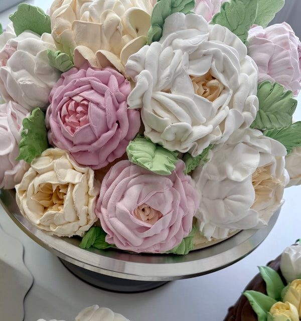 Close-up of a flower bouquet cake with marshmallow roses in white, cream, and soft pink, with green leaves.