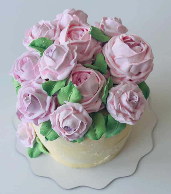 Top view of floral birthday cake with pink buttercream roses and green leaves arranged in a lush bouquet shape