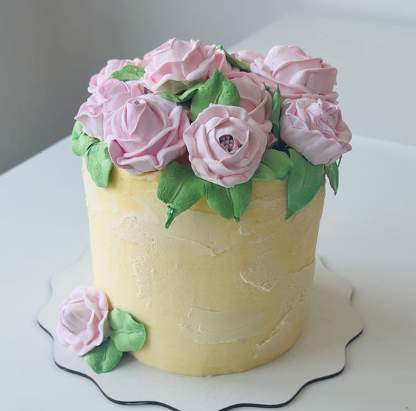 Buttercream cake topped with a crown of pink rose-shaped flowers and green leaves, with a matching flower on the base