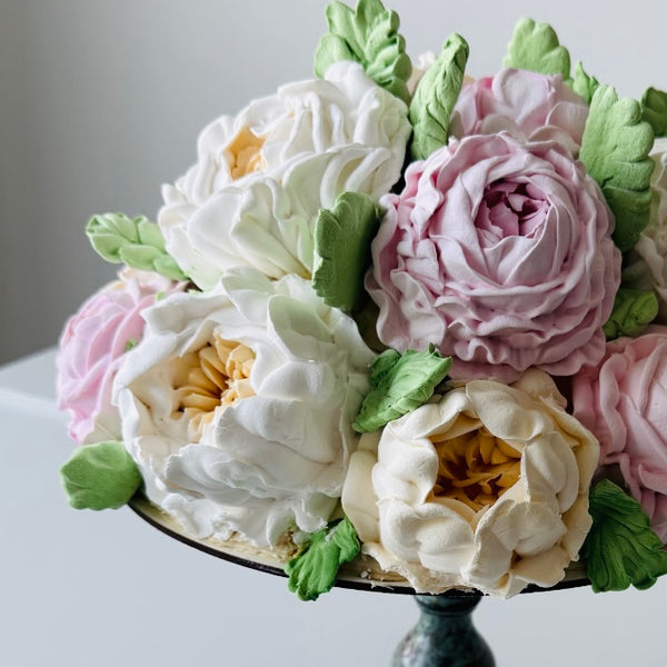 Close-up of realistic buttercream flowers in pastel shades of white, cream, yellow, and pink arranged like a floral bouquet.