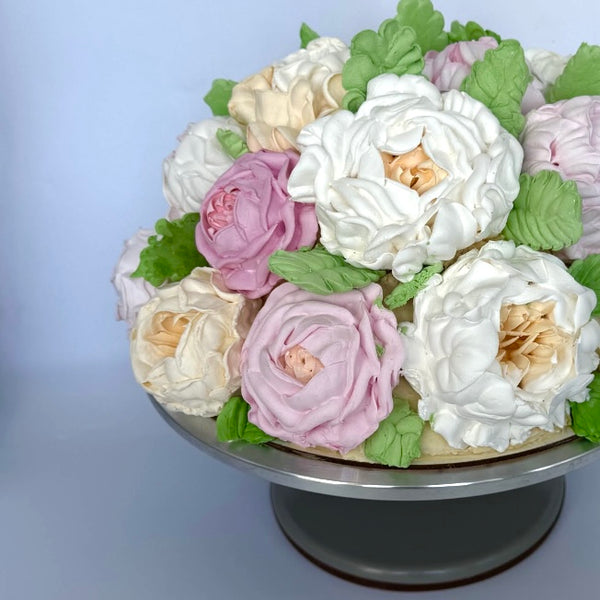 Floral cake arranged like a bouquet with white, cream, and pink marshmallow roses and green leaves in a bowl.