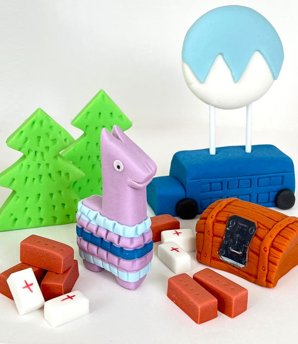 Set of colorful edible cake toppers inspired by Fortnite, featuring a llama piñata, evergreen trees, a blue bus, medkits, building bricks, and a treasure chest.