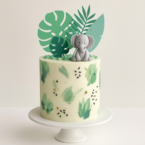 “Jungle-inspired cake with green brush strokes, fondant elephant topper, and tropical paper leaves, perfect for baby showers or birthdays.”
