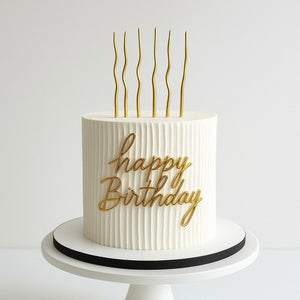 “Minimalist white birthday cake with vertical stripe texture, golden wavy candles, and ‘Happy Birthday’ in gold script.