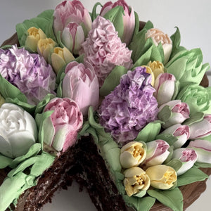 Chocolate cake decorated with colorful buttercream tulips and other spring flowers, one slice cut out.
