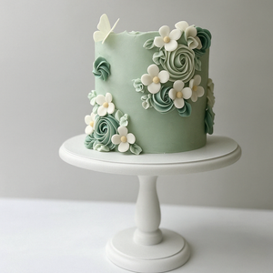 Sage green fondant cake adorned with handmade white and green sugar flowers and a white butterfly on top.
