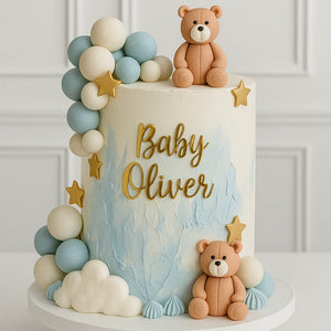 Elegant baby shower cake with blue and white watercolor design, decorated with fondant teddy bears, clouds, stars, and pastel balloons, personalized with ‘Baby Oliver’ in gold lettering