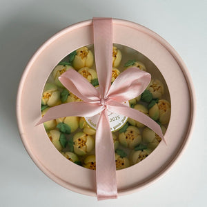 Round gift box with pink ribbon and green and yellow flowers inside.