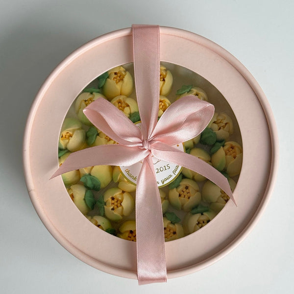 Round gift box with pink ribbon and green and yellow flowers inside.