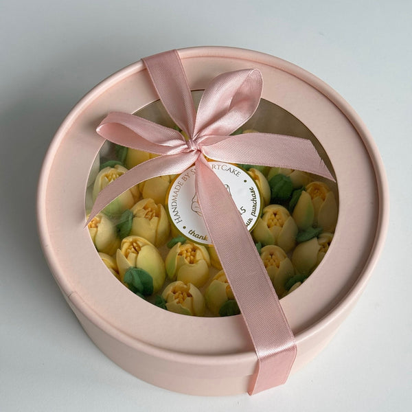 Round pink gift box with marshmallow flowers, yellow tulips  and a pink ribbon on a light gray background
