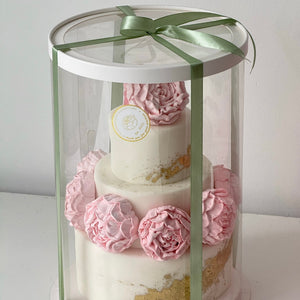 handmade two-tier marshmallow flower cake with pink decorations in tall clear gift box with green ribbon