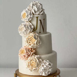 handmade three-tier white cake with marshmallow flower decorations and gold initials on cake stand