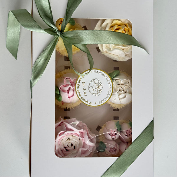 packaged cupcakes with marshmallow floral designs and a green ribbon on a white background