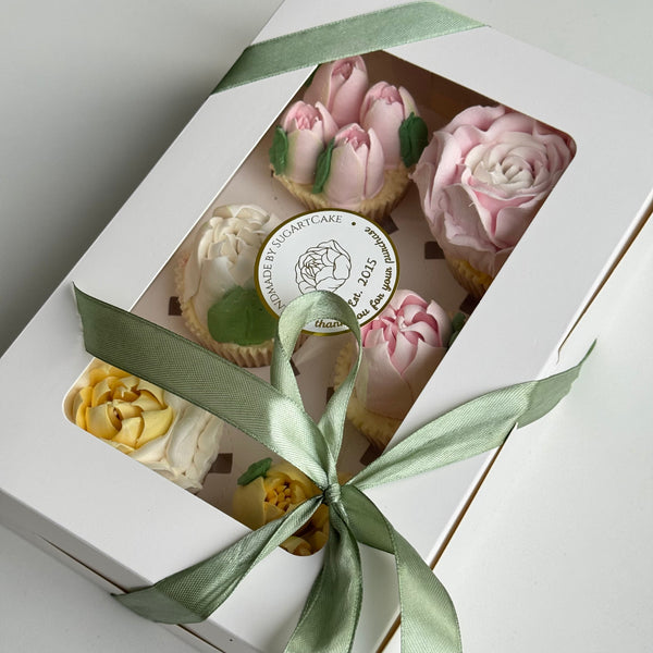 decorative box with pink marshmallow flowers cakes and a green ribbon on a white background
