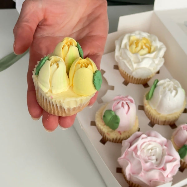 hand holding a cupcake decorated like a flower with more cupcakes in the background