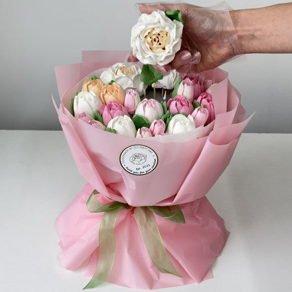 Bouquet of marshmallow flowers wrapped in pink paper with a green ribbon, held by a hand.