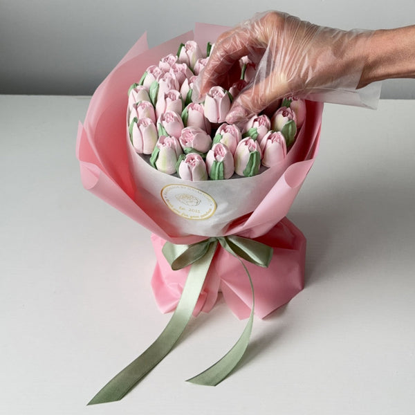 Handmade edible marshmallow tulip bouquet in pink wrapping with a gloved hand adjusting one flower