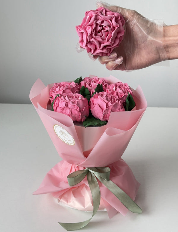 Bouquet of a handmade pink marshmallow flowers, peonies with a hand holding one flower, on a light gray background