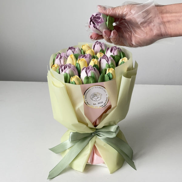 Handmade bouquet of marshmallow tulips with a hand wearing a glove holding a single flower in a light backgroud.