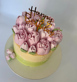 “Floral birthday cake with pink tulip-like buttercream flowers and green accents, featuring a ‘Happy Birthday’ topper.”