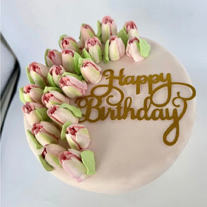 Elegant birthday cake with pink tulip-like buttercream flowers and gold "Happy Birthday" text.