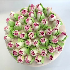 Round cake decorated with realistic pink and white tulip-shaped cream flowers on top