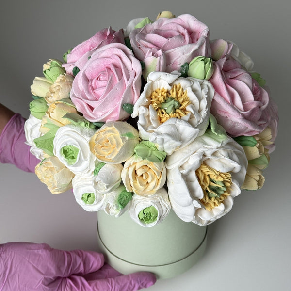 handmade marshmallow flower bouquet cake with pink, white and yellow blooms and green leaves arranged in a pastel green box, held in gloved hands