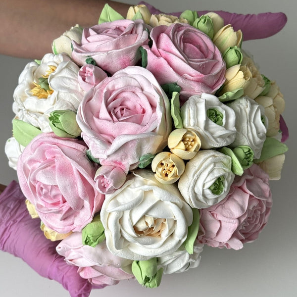 close-up of a handmade marshmallow flower bouquet with pink, white and yellow blooms and green leaves held in gloved hands