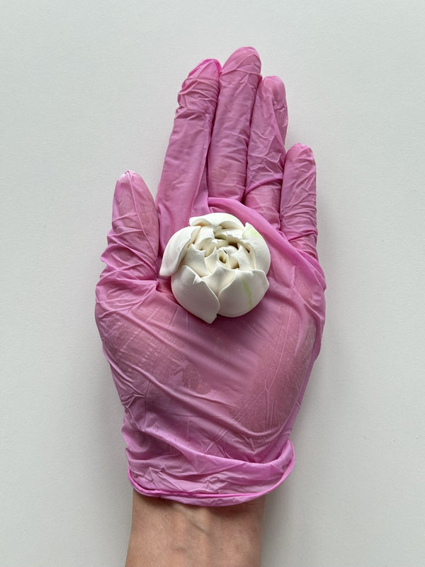 Pink glove holding a white flower-like object against a light gray background