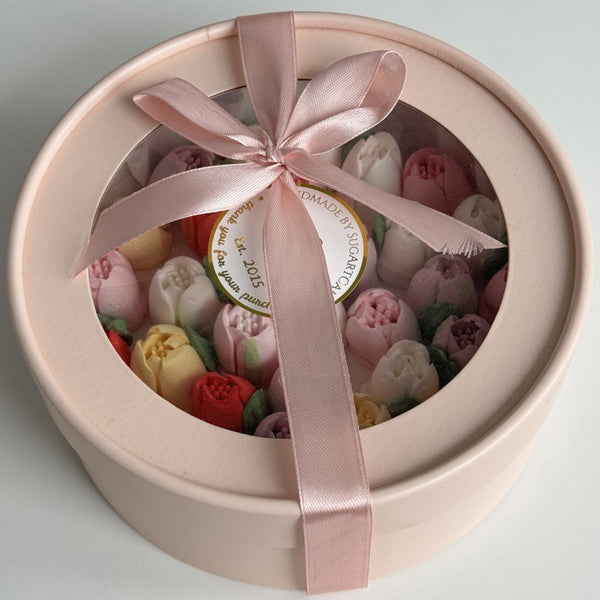 Round gift box with pink ribbon containing small flowers, on a light gray background