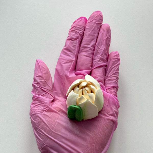 Pink glove holding an edible white marshmallow tulip on a light grey background