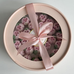 Round gift box with pink flower cake toppers and a pink ribbon on a light gray background