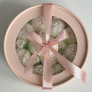 Round gift box with pink ribbon and white tulips on a light gray background