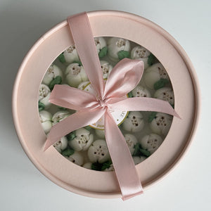Round gift box with pink ribbon filled with small white tulips and green leaves on a light gray background