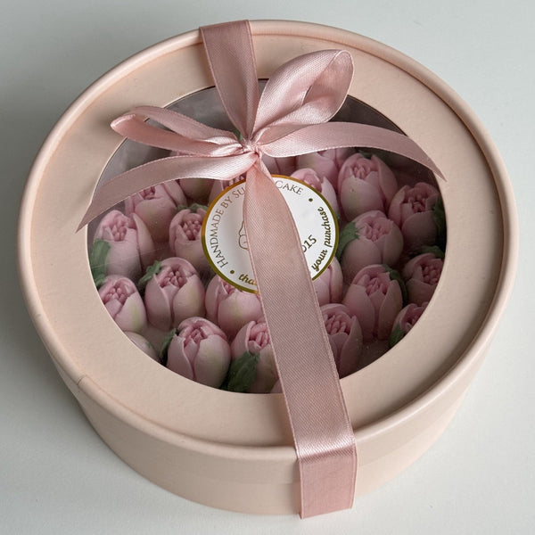Round pink box with sugar tulip flowers and a pink ribbon on a light gray background