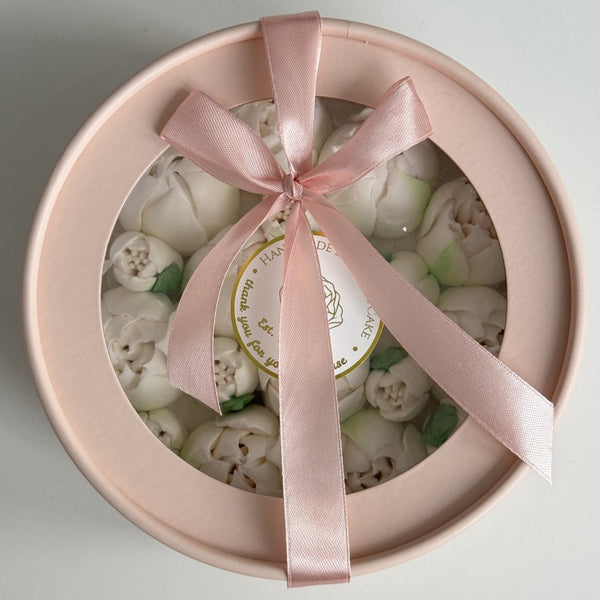 Round gift box with pink ribbon and edible flowers inside on a light gray background