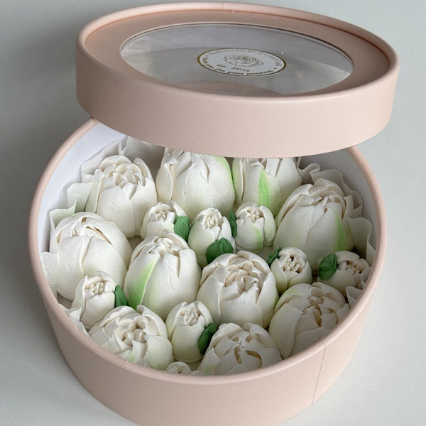 Round pink box containing handmade white tulips s on a light gray background